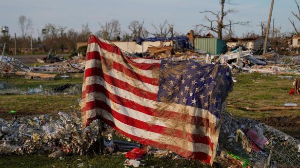 Et mudret amerikansk flag dækker ødelagte bygningsdele efter en tornado i Mississippi, som er USA’s fattigste stat.
