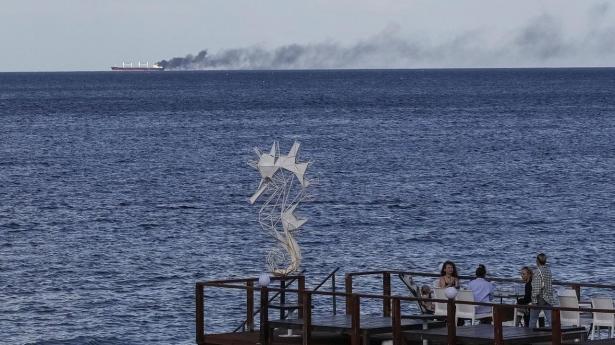 Caféstemning fra den ukrainske havneby Odesa, mens et brændende handelsskib i baggrunden er ramt af russiske droner.