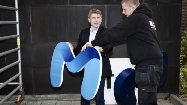 Ole Folmer, ejer af Mobitel. Her med det nye logo, der skal erstatte det gamle TDC-logo på bygningen, og som netop er ved at blive sat op af skiltemontører. Foto: Kristine Kiilerich