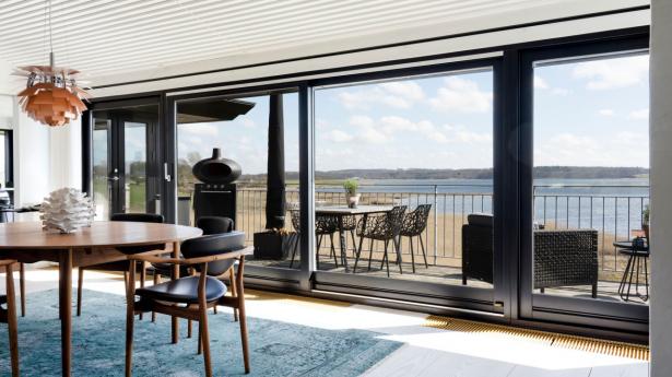 Mellem det skulpturelle ildsted og vinduespartiet mod fjorden og Munkholmbroen i det fjerne har familien indrettet hjemmets spisestue. Her er Finn Juhls Judasbord omkranset af samme designers stole, FJ109. I bordpladen er der nedfældet 30 plaketter af sterlingsølv, og af denne grund bliver bordet kaldt Judasbordet. Over bordet hænger PH’s kogle i messing, og på bordet ses en keramikskulptur af Hanne Lysdahl Christiansen. Gulvtæppet er fundet i Illums Bolighus. Den sorte krukke ved ildstedet er fra Muubs, og flodhesten over er en gave købt i Afrika. Øverst står en skulptur af naturkunstneren Mogens Grønbæk, en nær ven af huset, som familien har samarbejdet med i mange år på blandt andet restaurant Suri.