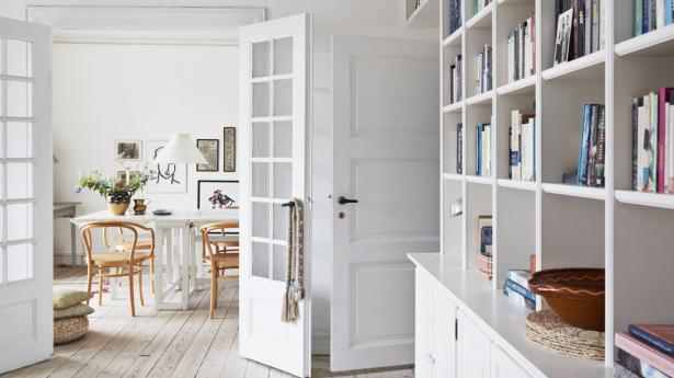 Ned langs reolerne i stuen ligger en blå uldløber på de rå bræddegulve. Her ses mod spisestuen.