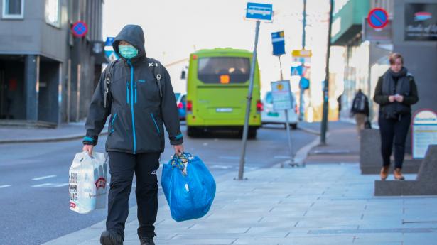 En mand med maske for ansigtet bærer sine indkøbsposer hjem gennem Oslos næsten tomme gader. De barer og restauranter i byen, der stadig har åbent, overholder ikke i tilstrækkelig grad reglerne om blandt andet at holde en meters afstand mellem de tilstedeværende - så nu forbyder bystyret salg af alkohol i et forsøg på at begrænse antallet af gæster.