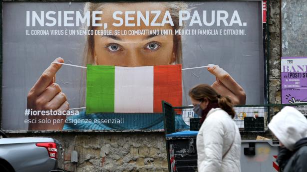 To italienere går forbi et billboard med teksten "Alle sammen, uden frygt" i byen Napoli søndag. Italiens premierminister, Giuseppe Conte, har søndag beordret al ikke-nødvendig produktion indstillet og virksomheder lukket, medmindre deres arbejde er uundværligt. På en måned er 5476 mennesker, der var smittet med coronavirus, døde i Italien.