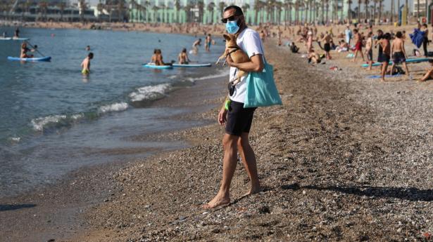 En mand med maske nyder solen på Barceloneta-stranden i Barcelona torsdag. Endnu har Spanien ikke åbnet for turister.