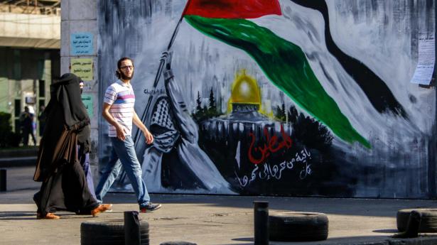 En mand og en kvinde i byen Tripoli i det nordlige Libanon går forbi et murmaleri, der viser en maskeret demonstrant med et palæstinensisk flag ved Klippemoskéen i Jerusalem. Den libanesiske Hizbollah-bevægelse har bånd til Hamas i Gaza. Torsdag er der affyret tre raketter over grænsen til Israel, men ingen har endnu taget skylden for angrebet.