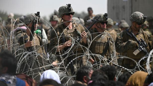 Amerikanske soldater holder vagt bag pigtråd, mens tusinder af afghanere har sat sig på en vej udenfor lufthavnen i Kabul, hvor de håber at kunne komme på et fly ud af landet.