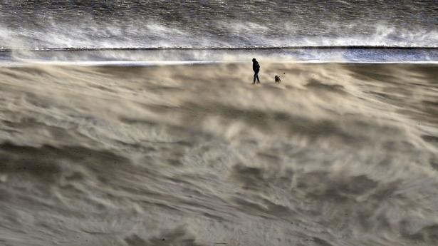 En hundelufter er ude på en tur ved stranden i Tynemouth i det nordlige England lørdag, inden stormen tog til i styrke.