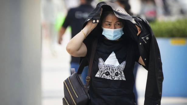 Kina har været ramt af ekstrem varme i år. Her beskytter en kvinde sig mod solens stråler med sin jakke, mens hun går gennem en shoppinggade i den kinesiske hovedstad, Beijing, i juni i år, hvor temperaturen har været op mod 37 grader. Foto: Mark Schiefelbein/Ritzau Scanpix
