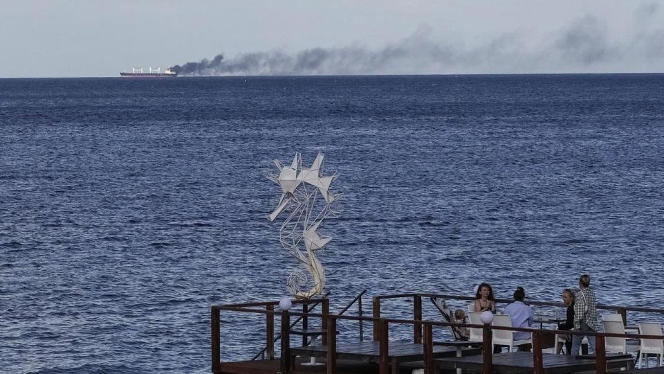 Caféstemning fra den ukrainske havneby Odesa, mens et brændende handelsskib i baggrunden er ramt af russiske droner.