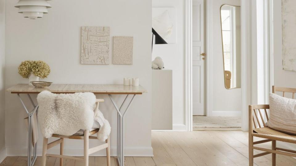Parrets mellemstue med udsigt mod terrassen og haven, som ligger højt og væk fra vejen. Og et kig til den lille gang, hvorfra der er adgang til bryggers og trappe til førstesal. Stuen fungerer forbindelse til den tilbygning, som huset fik i 2005. Gulvtæppe købt i Marrakech, skrivebordet er lavet med ben fra Broste Copenhagen, og værkerne over er af Kirsten Schrøder. Spejlet er fra Gubi.