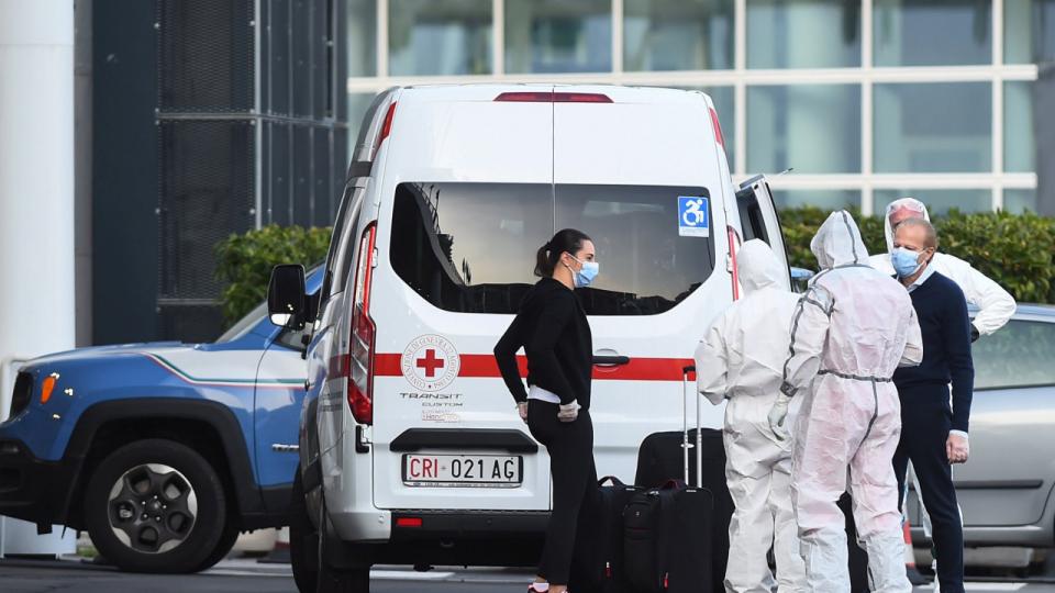 Passagerer fra krydstogtskibet Costa Luminosa, som var ramt af coronasmitte, ledsages fra skibet til en ambulance af sundhedspersonale i beskyttelsesdragter. Skibet har lagt til i havnen i byen Savona tæt ved Genova i det nordlige Italien.