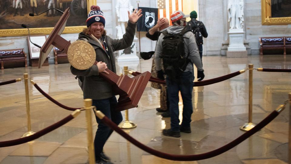 Den 36-årige Adam Christian Johnson fotograferet onsdag på vej gennem rotundaen i USA's kongresbygning. I armene har han den stjålne talerstol, der tilhører formanden for Repræsentanternes Hus, Nancy Pelosi.